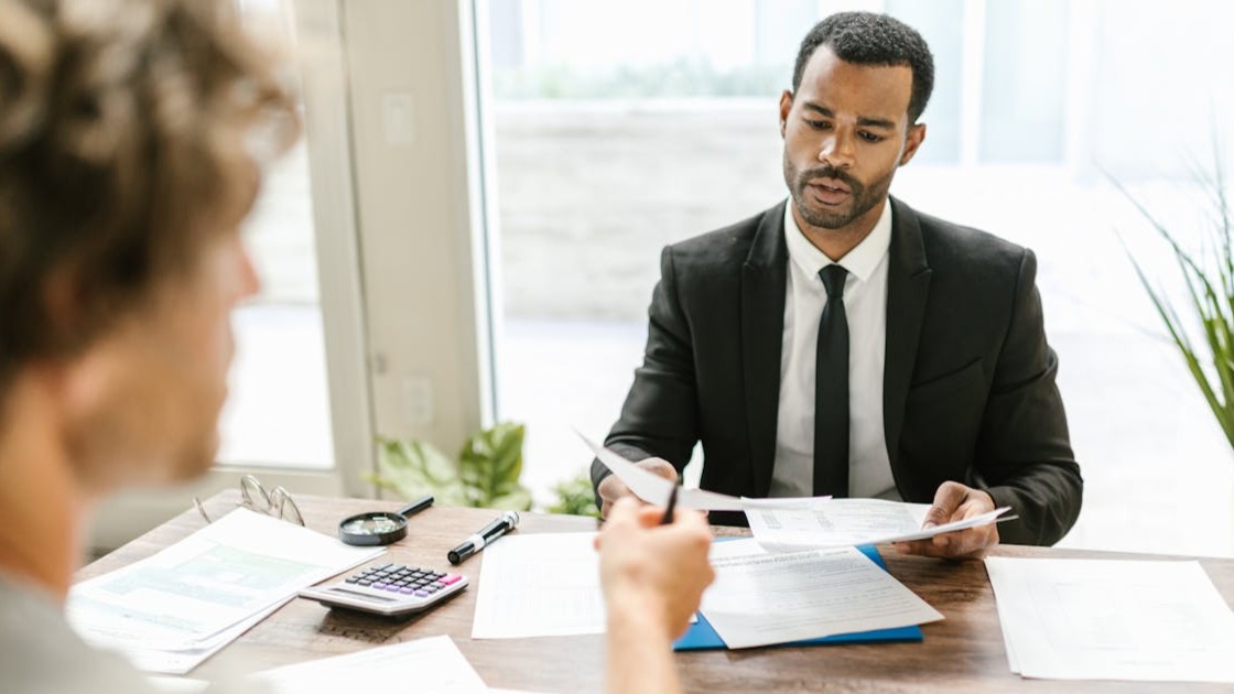 Business professional conducting a job interview at a desk, reviewing documents and evaluating a candidate’s answers.